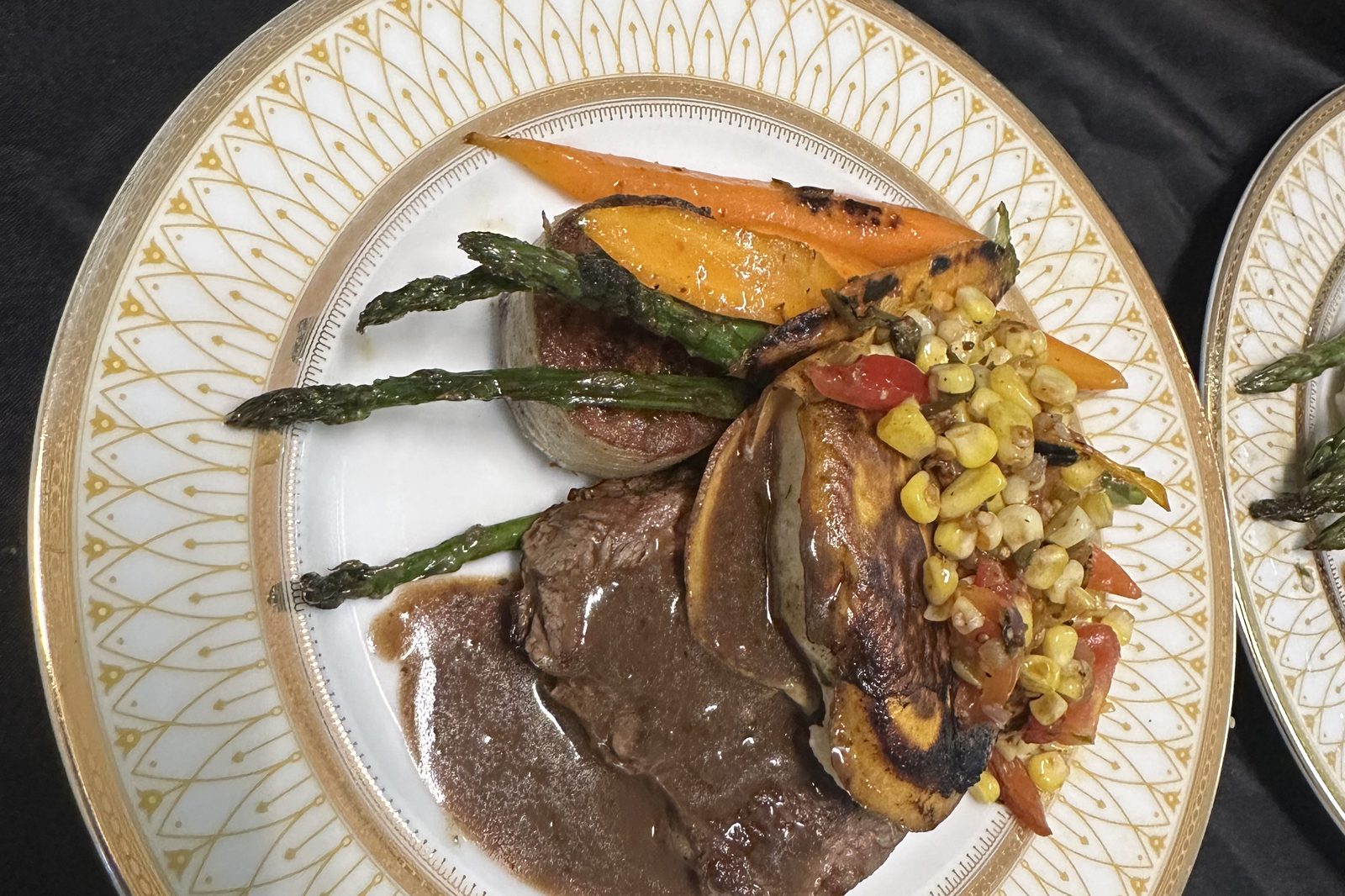 Plated steak entree with roasted vegetables and corn relish, served on gold rimmed china at a B Hospitality Group private dinner